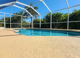 Freshly painted textured cool-deck pool deck around a screened pool in a South Florida backyard