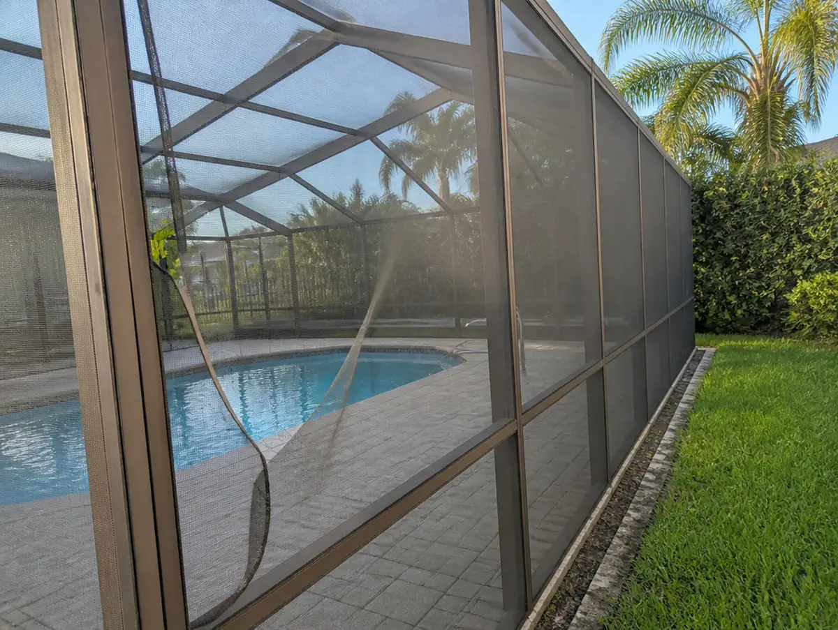 Torn screen panel pulling loose from an aluminum pool cage enclosure in South Florida