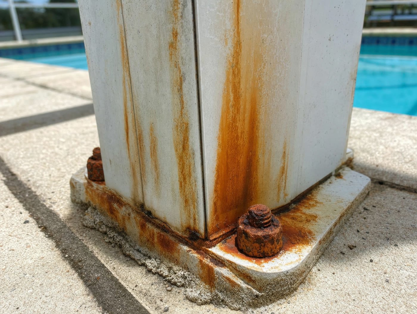 Corroded rusty anchor bolt and rust stained base plate at the bottom of a Florida pool cage upright
