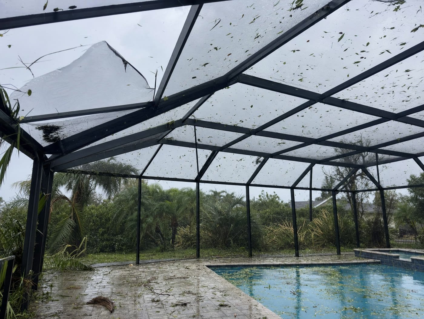Storm debris and palm fronds resting on the screened roof of a Florida pool cage after a hurricane