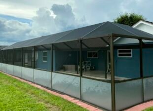 Restored bronze pool cage with new screen and privacy panels along the lower section, attached to a blue house
