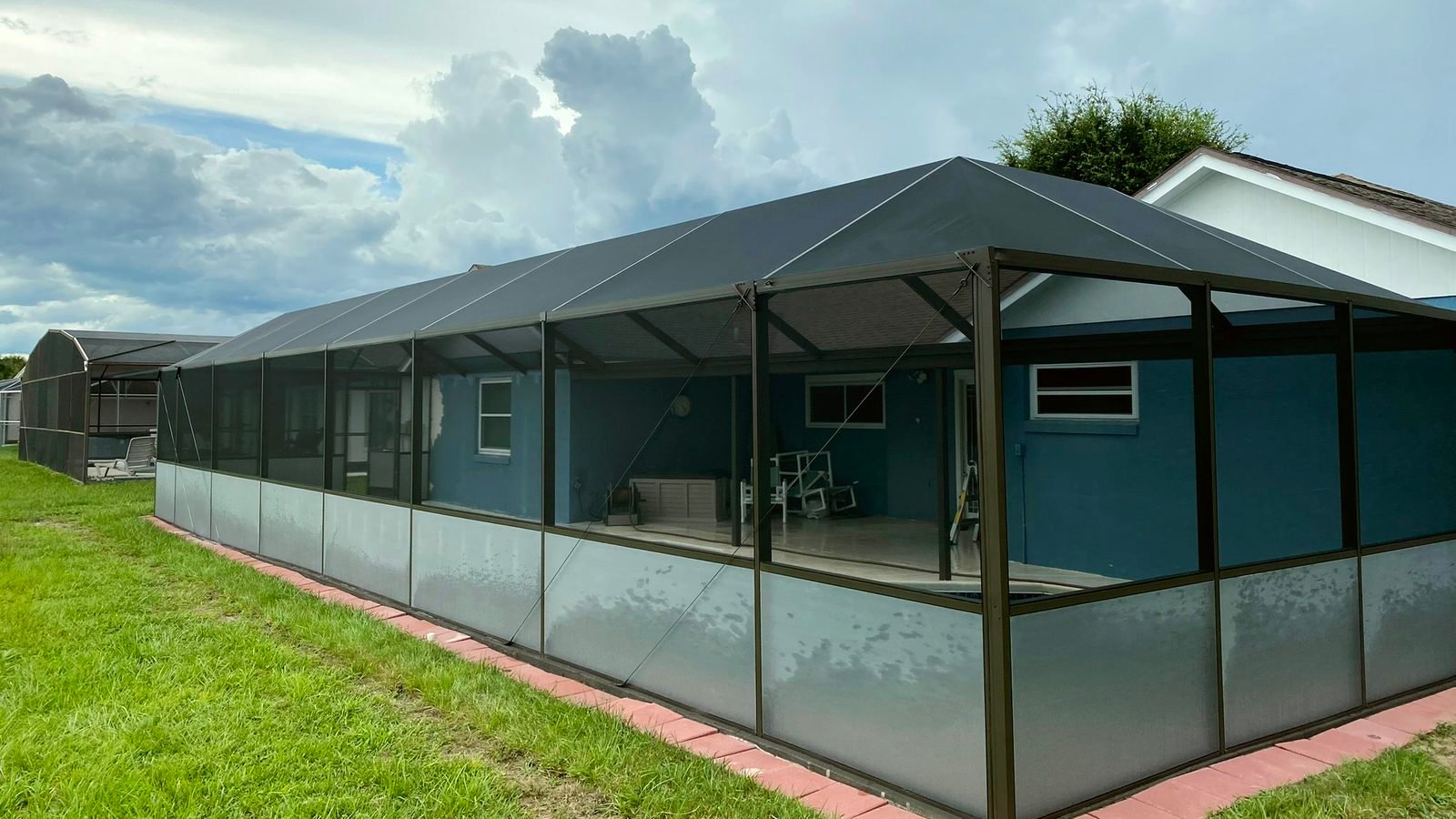 Restored bronze pool cage with new screen and privacy panels along the lower section, attached to a blue house