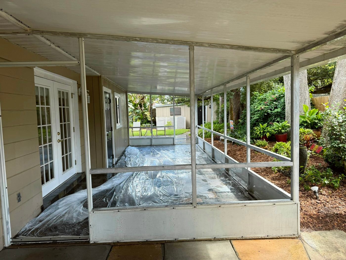 Screen porch with the screens removed and plastic sheeting over the floor before the white aluminum frame is painted