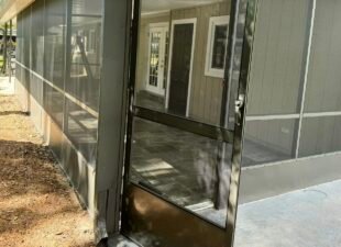 Dark bronze screen door swung open on a screened porch, with a solid kickplate across the bottom and a latch handle