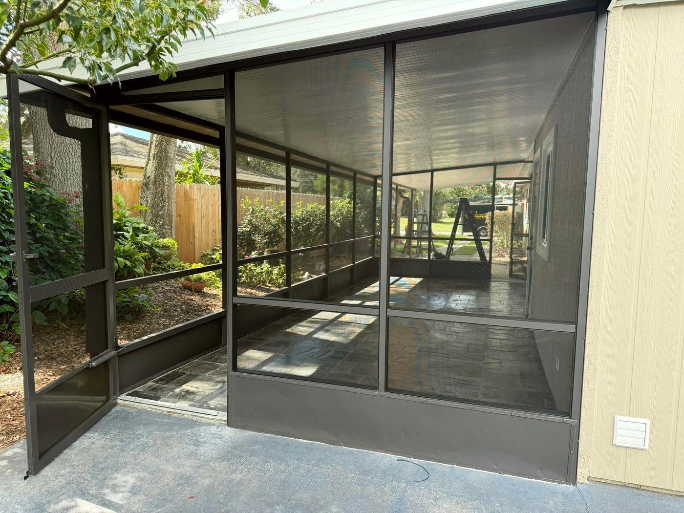 Open dark bronze screen door with a closer mounted near the bottom and a solid kickplate across the lower panel